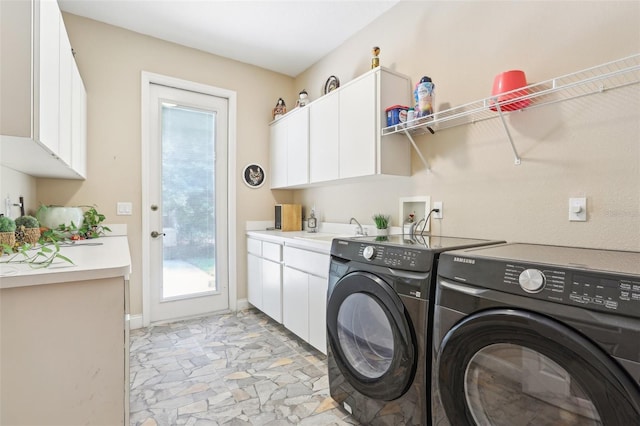 clothes washing area with washing machine and dryer, baseboards, stone finish flooring, a sink, and cabinet space