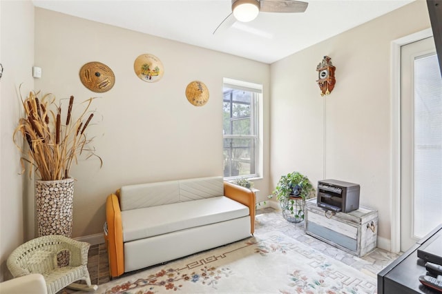 living area with baseboards and ceiling fan