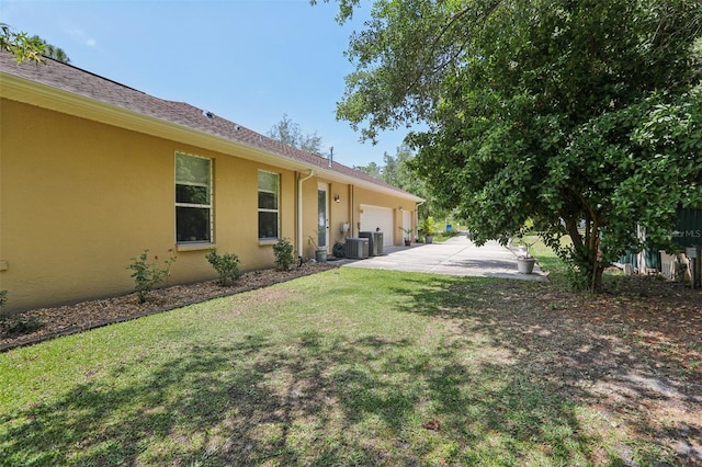 view of yard with central AC unit, driveway, and an attached garage