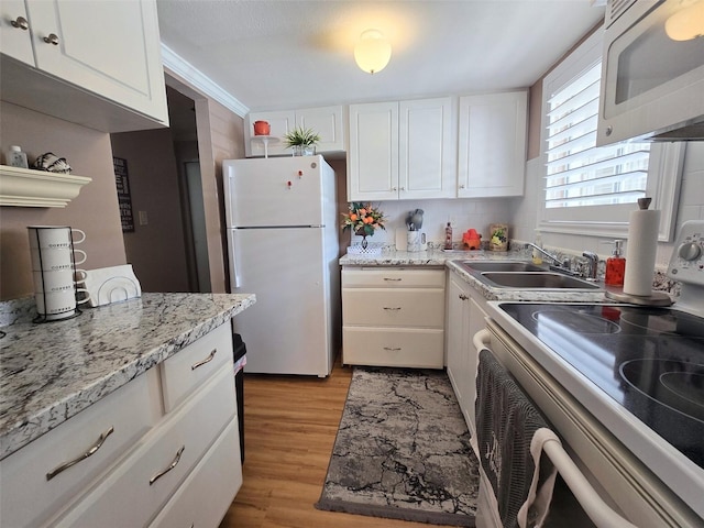 kitchen featuring a sink, light wood finished floors, white appliances, and white cabinetry