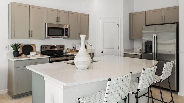 kitchen with stainless steel appliances, a kitchen breakfast bar, light countertops, light tile patterned floors, and gray cabinetry