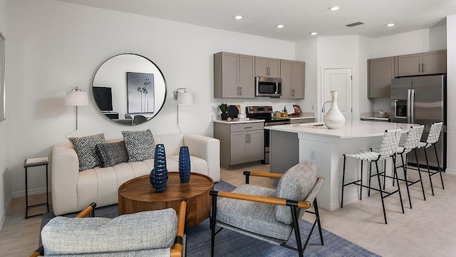 kitchen featuring gray cabinetry, visible vents, a kitchen bar, open floor plan, and stainless steel appliances