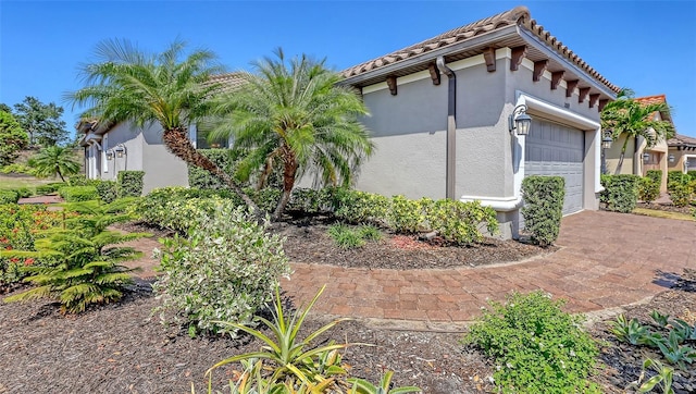 view of side of home featuring stucco siding, a tiled roof, an attached garage, and driveway