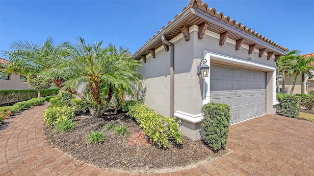 view of home's exterior with stucco siding, an attached garage, decorative driveway, and a tiled roof