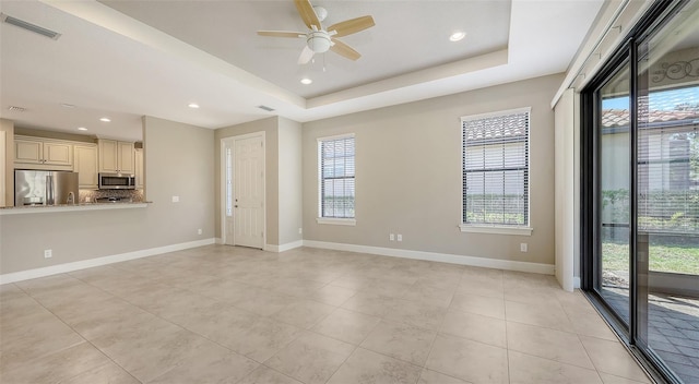 unfurnished living room featuring a ceiling fan, light tile patterned flooring, baseboards, recessed lighting, and a tray ceiling