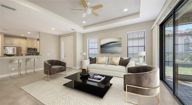 living room with light tile patterned floors, a ceiling fan, recessed lighting, baseboards, and a tray ceiling