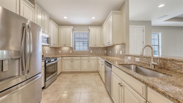 kitchen with appliances with stainless steel finishes, a sink, plenty of natural light, light stone countertops, and recessed lighting