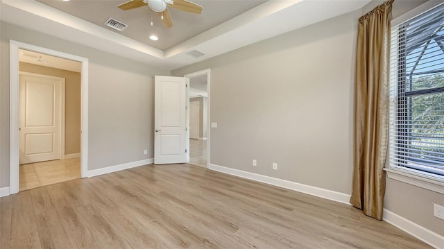 unfurnished bedroom featuring baseboards, a tray ceiling, light wood finished floors, recessed lighting, and ceiling fan