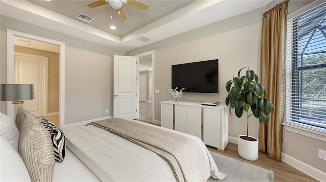 bedroom with baseboards, light wood-style floors, a raised ceiling, recessed lighting, and a ceiling fan