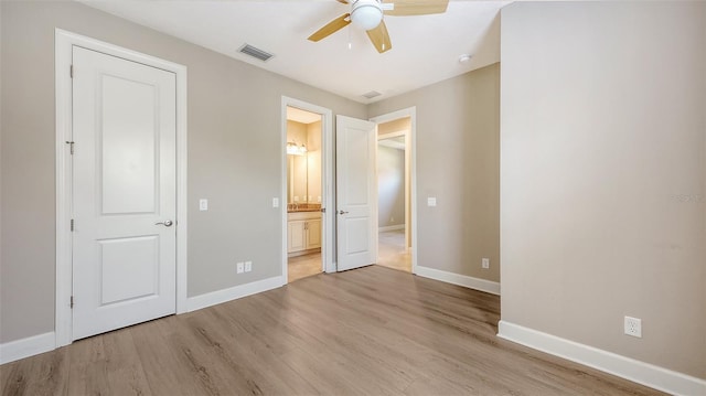 unfurnished bedroom featuring light wood-style flooring, baseboards, and connected bathroom