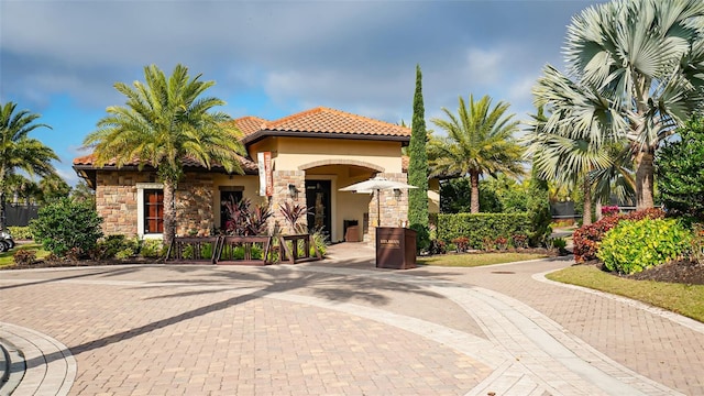 mediterranean / spanish-style house with stone siding, a tile roof, and stucco siding