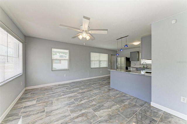 kitchen featuring freestanding refrigerator, gray cabinets, ceiling fan, baseboards, and a peninsula