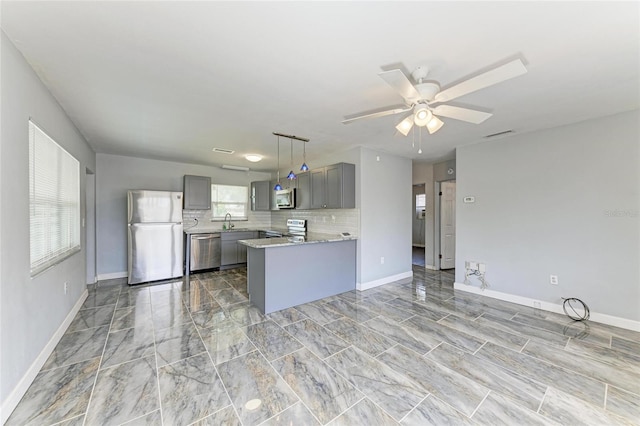 kitchen with stainless steel appliances, gray cabinets, a ceiling fan, baseboards, and a sink