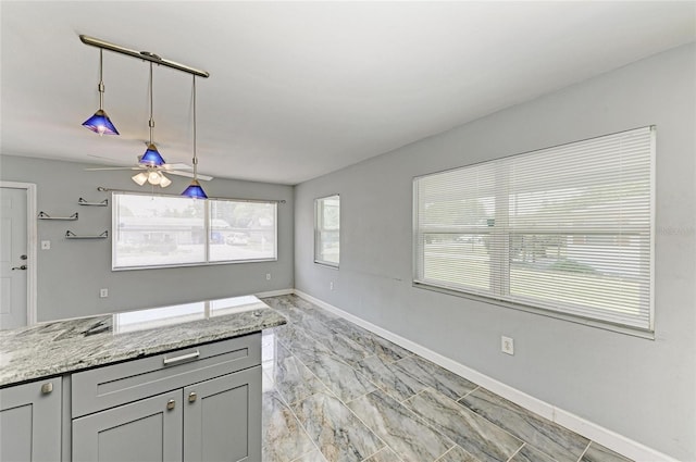 kitchen featuring light marble finish flooring, a ceiling fan, baseboards, pendant lighting, and light stone counters