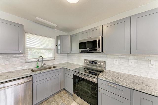 kitchen featuring stainless steel appliances, gray cabinetry, a sink, and backsplash