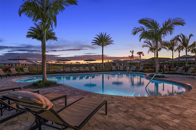 pool at dusk with a patio area, fence, and a community pool
