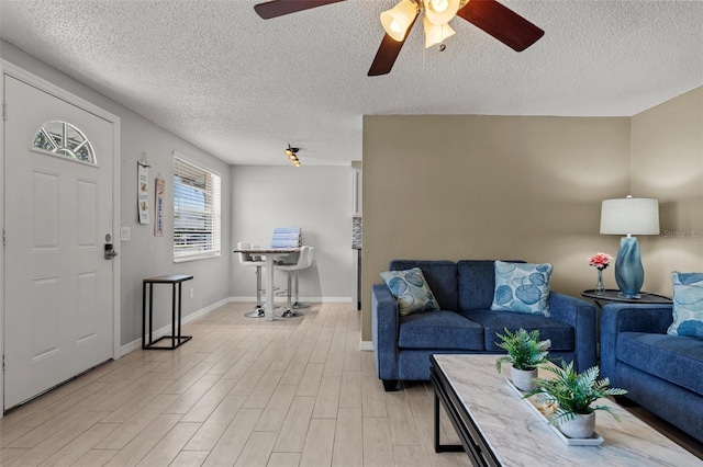 living area featuring light wood-style floors, a ceiling fan, a textured ceiling, and baseboards