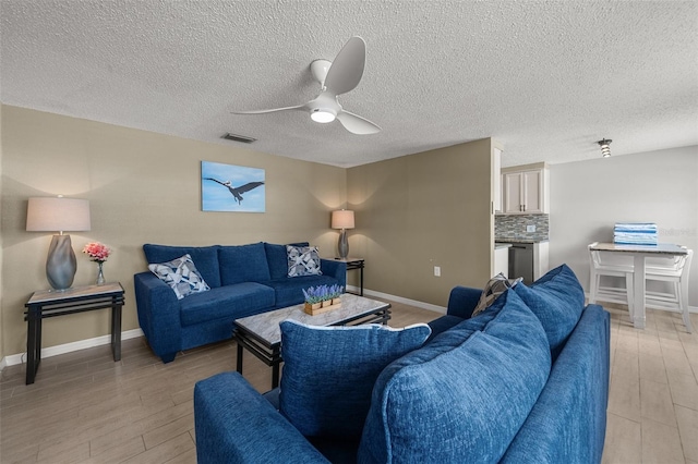 living room with light wood-style flooring, ceiling fan, baseboards, and a textured ceiling