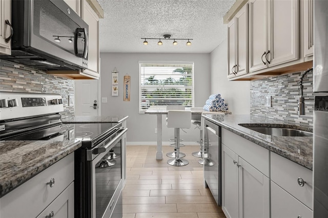 kitchen featuring appliances with stainless steel finishes, tasteful backsplash, stone counters, baseboards, and a textured ceiling