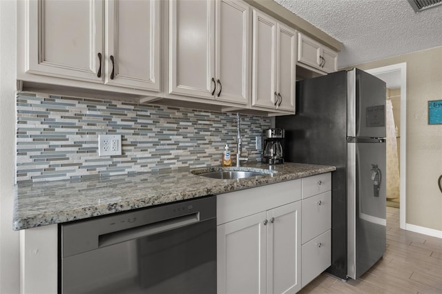 kitchen with appliances with stainless steel finishes, a sink, tasteful backsplash, light stone countertops, and light wood-style flooring