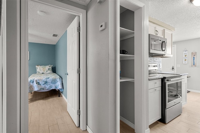 hallway featuring a textured ceiling, light wood-style floors, and baseboards