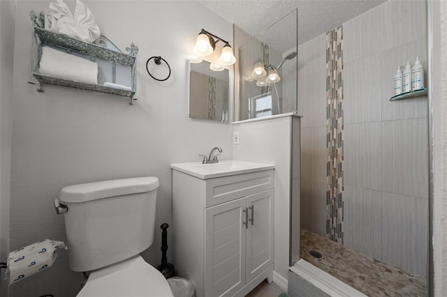 bathroom with toilet, a textured ceiling, a tile shower, and vanity