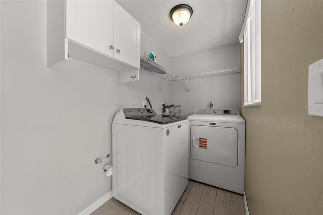laundry area featuring washer and clothes dryer, cabinet space, a textured ceiling, light wood-type flooring, and baseboards