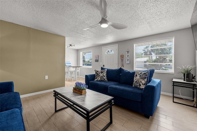 living room featuring light wood finished floors, ceiling fan, a textured ceiling, and baseboards