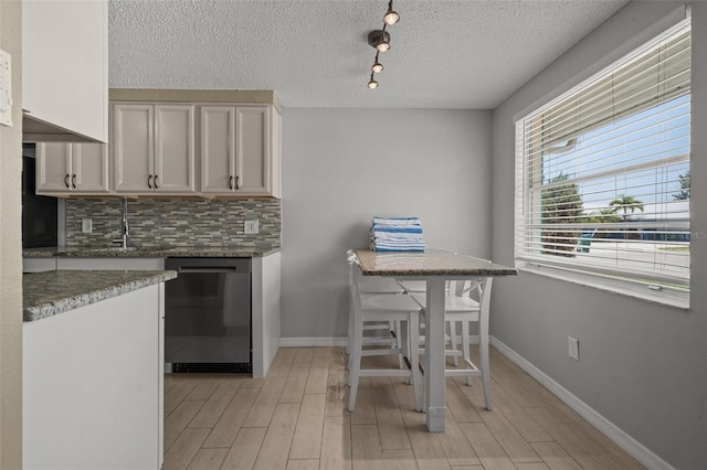 kitchen featuring dishwasher, tasteful backsplash, a textured ceiling, light wood finished floors, and baseboards