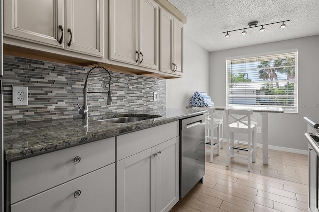 kitchen featuring dishwasher, a sink, decorative backsplash, a textured ceiling, and rail lighting