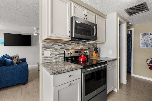 kitchen featuring stainless steel range with electric stovetop, a textured ceiling, open floor plan, tasteful backsplash, and light wood-style floors