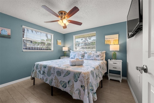 bedroom with wood finished floors, baseboards, a textured ceiling, and a ceiling fan