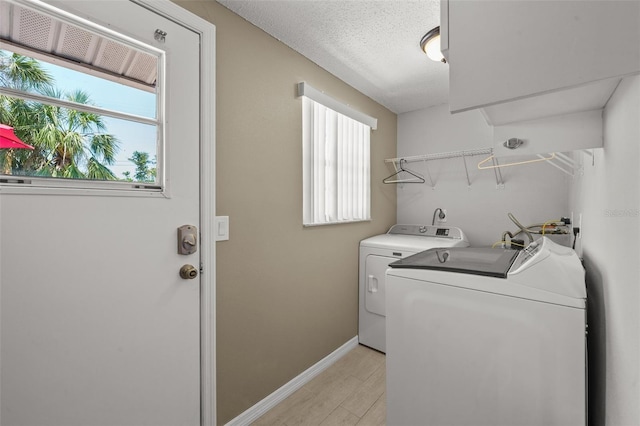 clothes washing area featuring independent washer and dryer, plenty of natural light, light wood-style floors, baseboards, and a textured ceiling