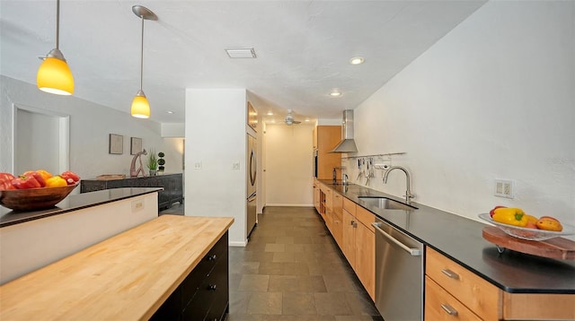 kitchen with appliances with stainless steel finishes, a sink, wall chimney range hood, butcher block countertops, and decorative light fixtures