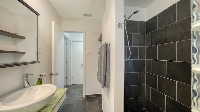 full bathroom with a sink, tiled shower, and tile patterned flooring