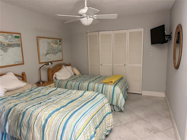 bedroom with a closet, a textured ceiling, light tile patterned flooring, baseboards, and ceiling fan