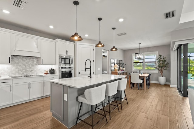 16226 Hidden Oak Loop, Bradenton, FL 34211 - kitchen featuring appliances with stainless steel finishes, premium range hood, tasteful backsplash, light wood-style flooring, and baseboards