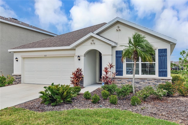mediterranean / spanish-style house with stone siding, a garage, driveway, stucco siding, and roof with shingles