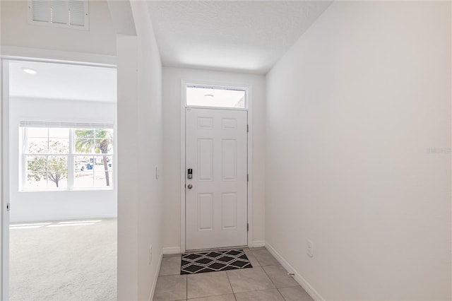 doorway featuring light tile patterned floors, baseboards, and a textured ceiling