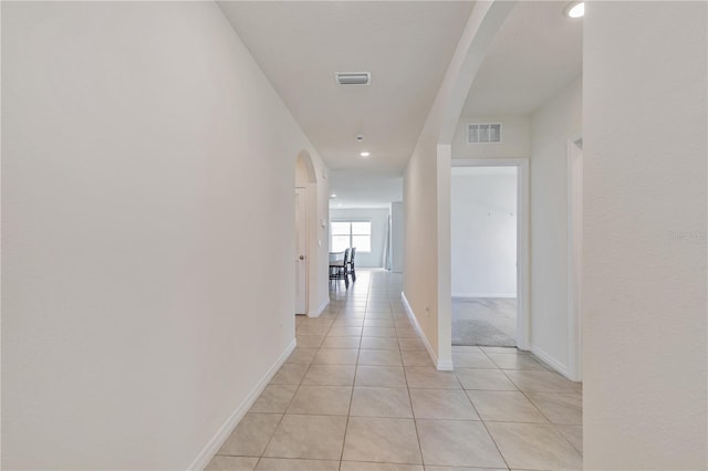 corridor with arched walkways, light tile patterned floors, baseboards, and recessed lighting