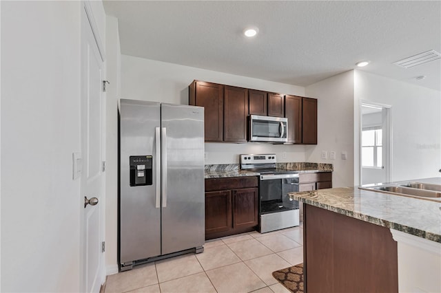 kitchen featuring appliances with stainless steel finishes, a sink, dark brown cabinets, light tile patterned floors, and a textured ceiling