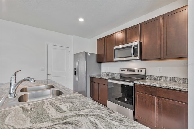 kitchen with stainless steel appliances, a sink, dark brown cabinets, recessed lighting, and light stone countertops