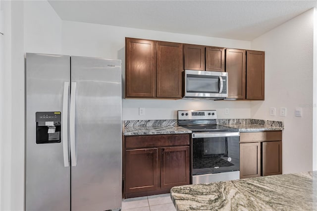 kitchen featuring appliances with stainless steel finishes, light stone counters, dark brown cabinets, and light tile patterned flooring