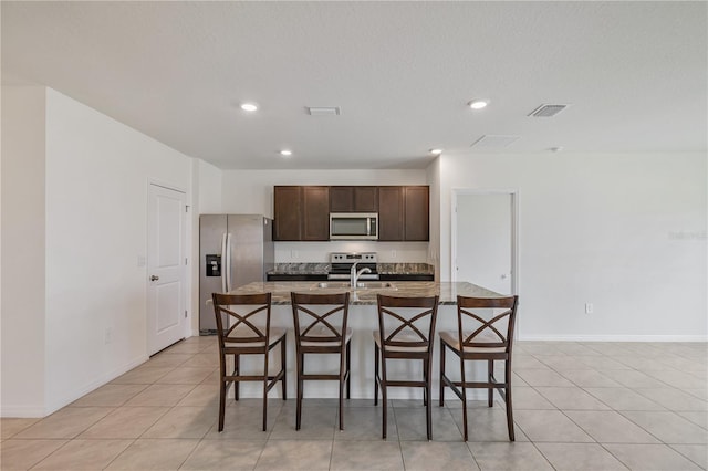 kitchen featuring appliances with stainless steel finishes, a kitchen breakfast bar, dark brown cabinetry, a kitchen island with sink, and light tile patterned flooring