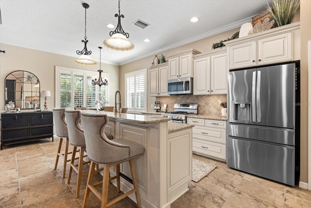 11508 Griffith Park Ter, Bradenton, FL 34211 - kitchen with appliances with stainless steel finishes, backsplash, light stone counters, hanging light fixtures, and a kitchen island with sink