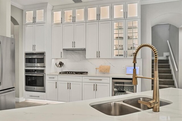 6470 Indigo Bunting Pl, Lakewood Ranch, FL 34202 - kitchen featuring stainless steel appliances, arched walkways, white cabinets, light stone counters, and crown molding
