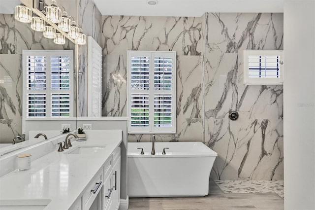 6470 Indigo Bunting Pl, Lakewood Ranch, FL 34202 - bathroom featuring double vanity, a freestanding tub, stone wall, and a chandelier
