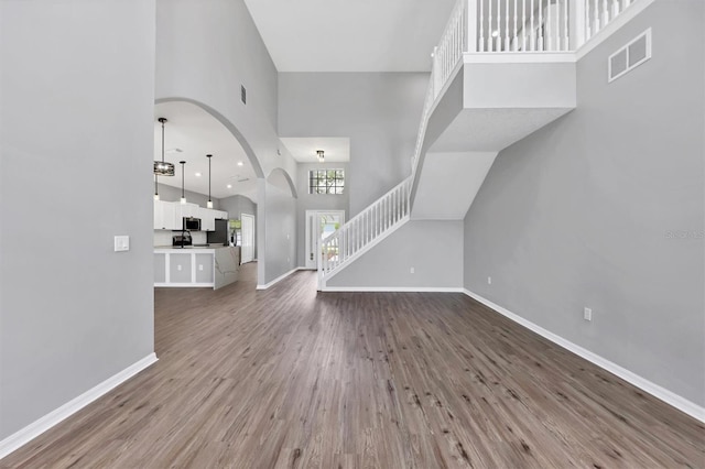 unfurnished living room with a towering ceiling, baseboards, stairway, wood finished floors, and arched walkways