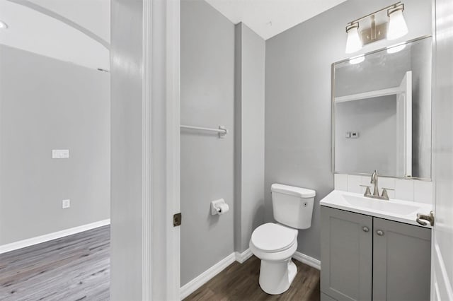 half bath with wood finished floors, toilet, vanity, and baseboards