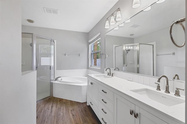 bathroom featuring a shower stall, a garden tub, double vanity, and wood finished floors
